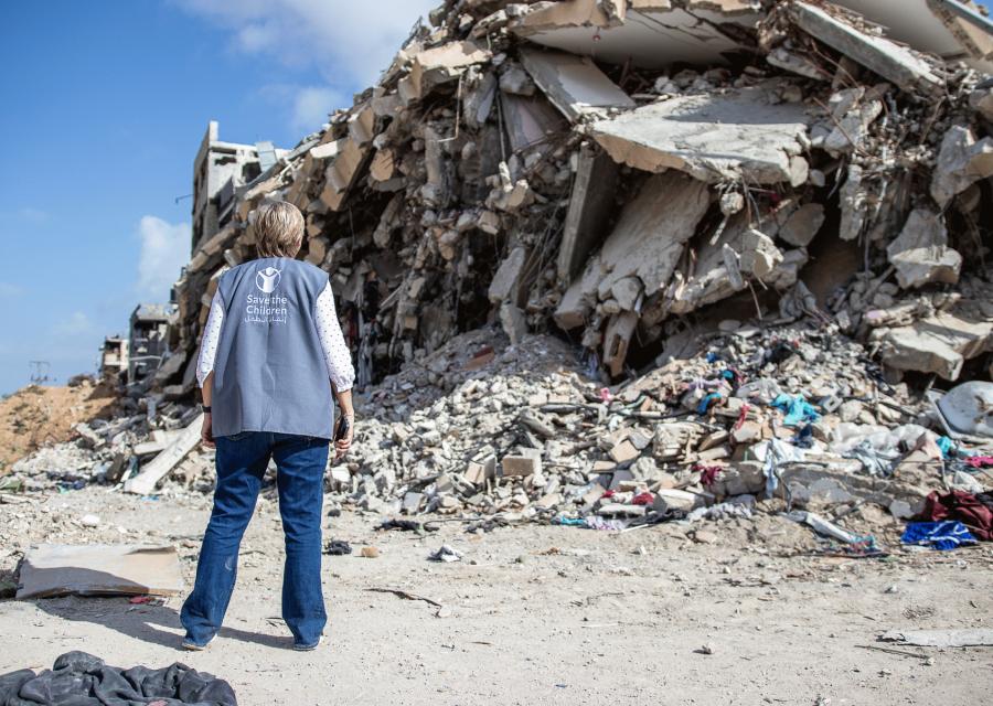 Operatrice umanitaria Save the Children di spalle di fronte a macerie 