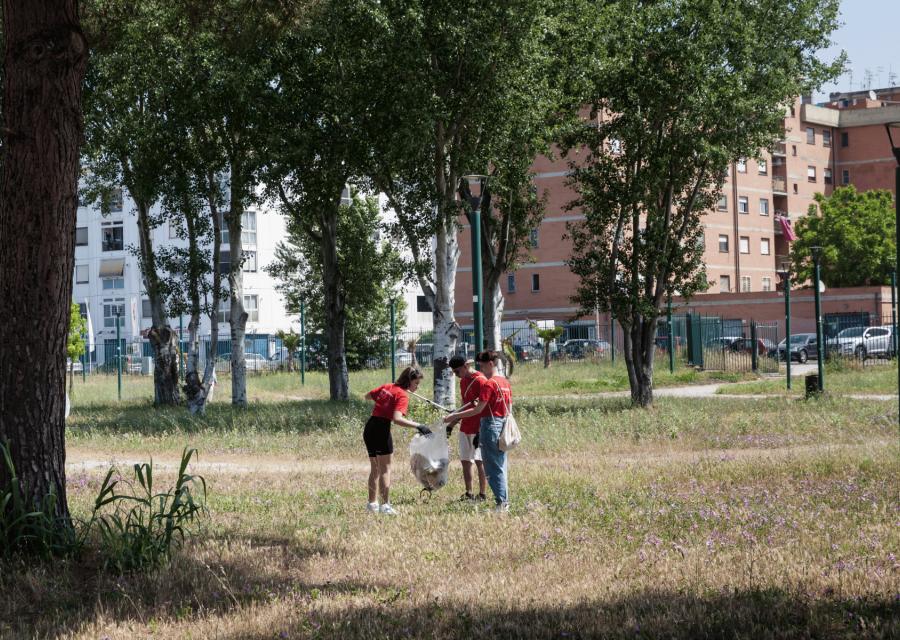 3 ragazzi che raccolgono immondizia in mezzo a un parco.