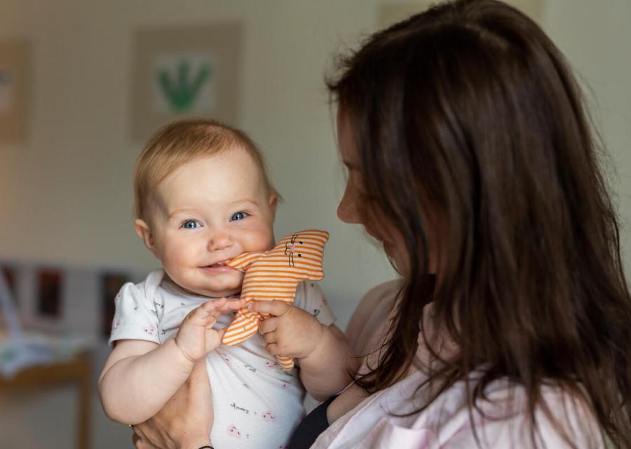Ragazza di spalle che tiene in braccio un bambino che sorride mentre more un pupazzo