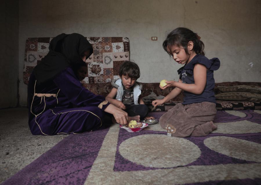 Famiglia di tre persone, composta da due bambini e una mamma, mangiando seduti per terra.