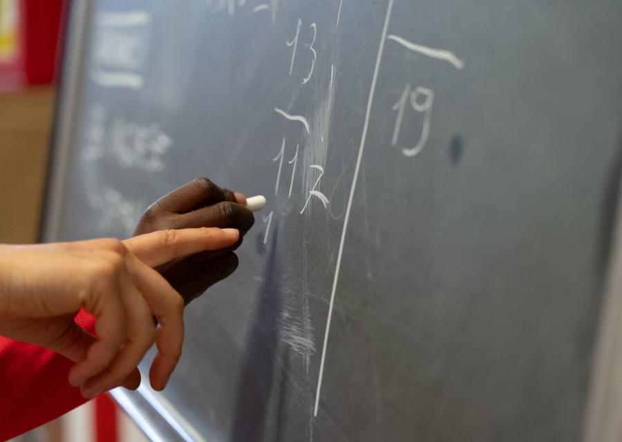 una lavagna con sopra scritti dei numeri e la mano di un bambino con il gessetto e una mano di un adulto 