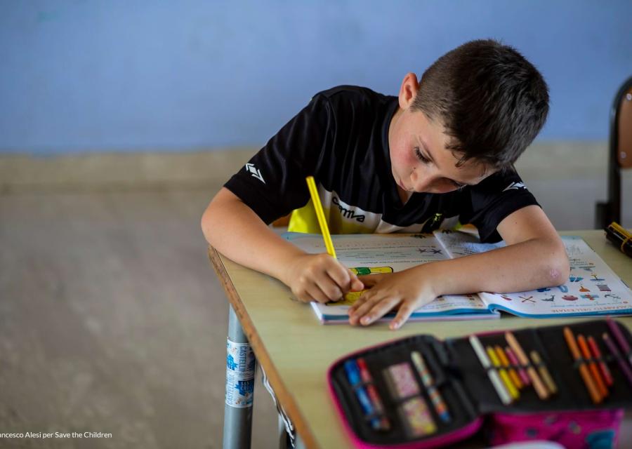 Bambino scrive con matita gialla seduto a un banco di scuola
