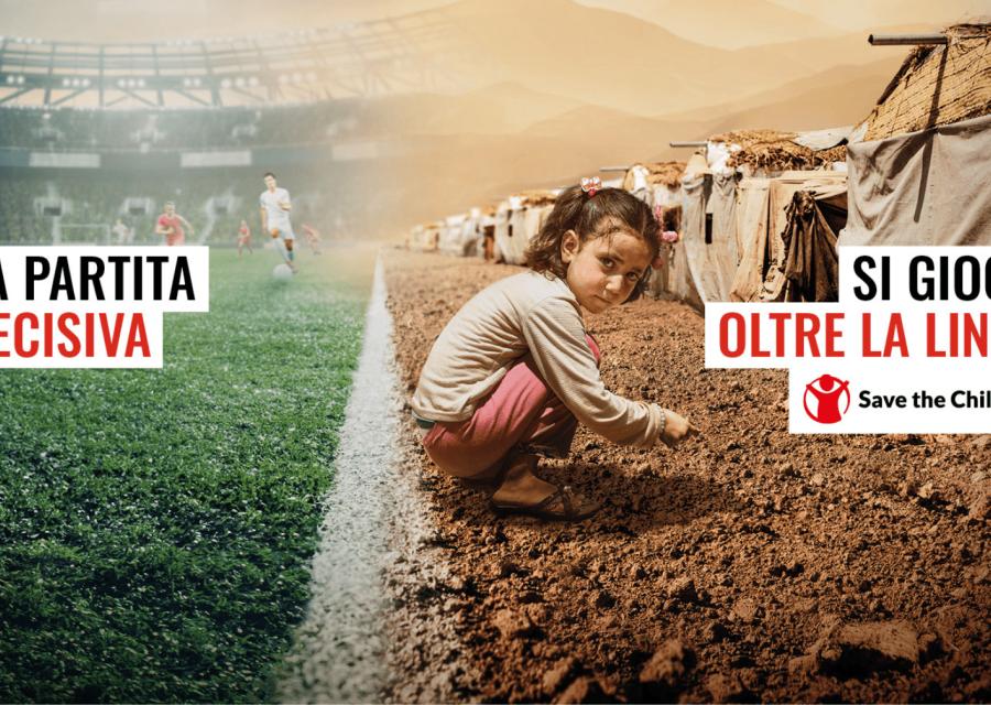 A sinistra bambina rannicchiata a bordo campo di calcio a destra calciatori sullo sfondo 