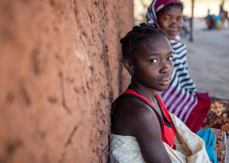 in primo piano ragazza in Mozambico seduta di spalle al muro di una casa