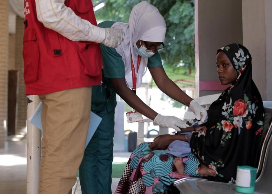 bambina seduta di lato che viene esaminata da due operatori si Save the Children 