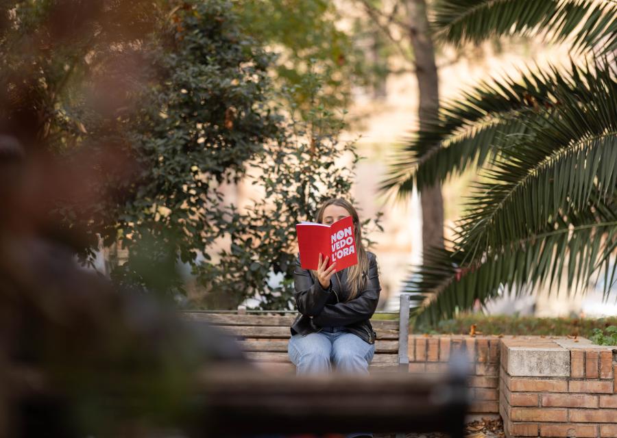 Ragazza legge libro rosso non vedo l'ora seduta su panchina 