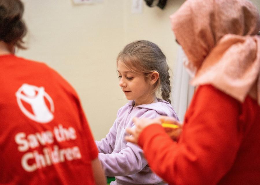 Due operatrici di Save the Children con una bambina
