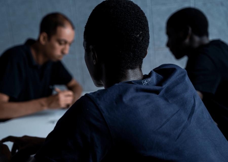 Due minori stranieri non accompagnati seduti ad un tavolo con un assistente che scrive