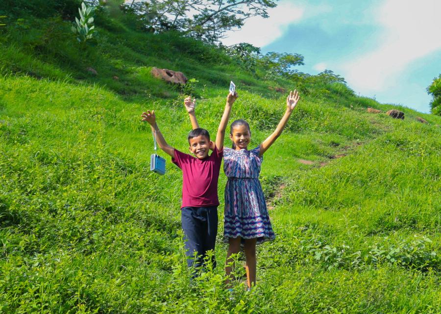 Bambino e bambina in un campo verde in El Salvador che sorridono con le mani in aria