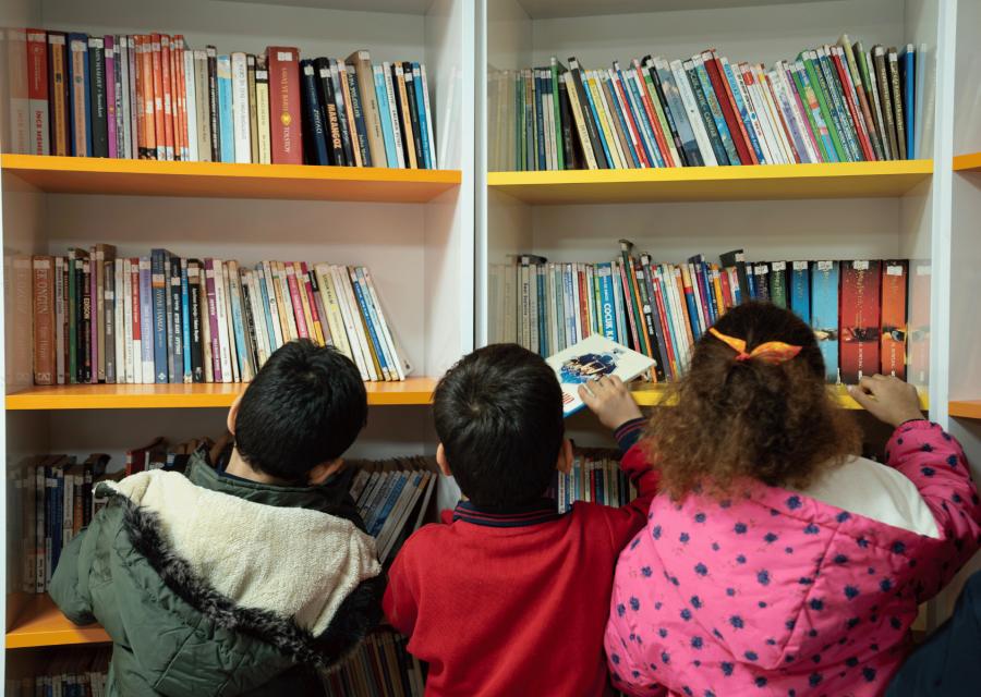 bambine  e bambini che guardano una parete con tanti libri colorati