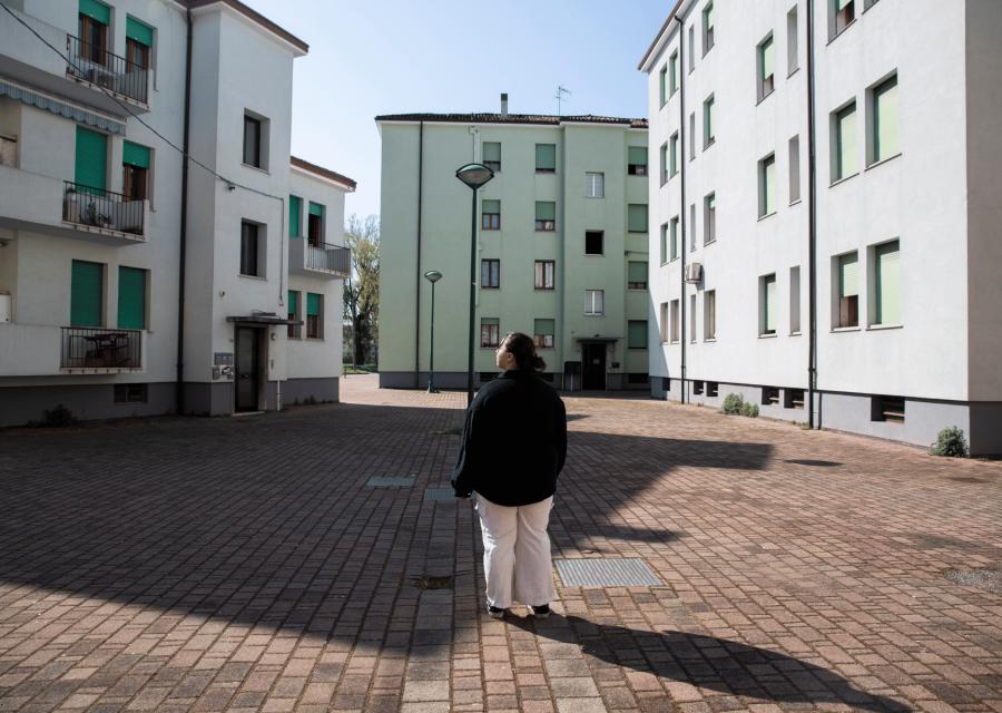 Al centro della foto, ragazza di schiena che guarda le case popolari dove vive