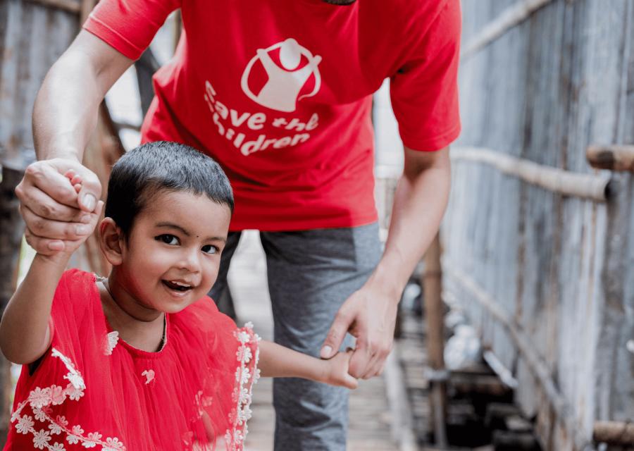 Bambina che sorride e tiene le mani ad una operatrice di Save the Children