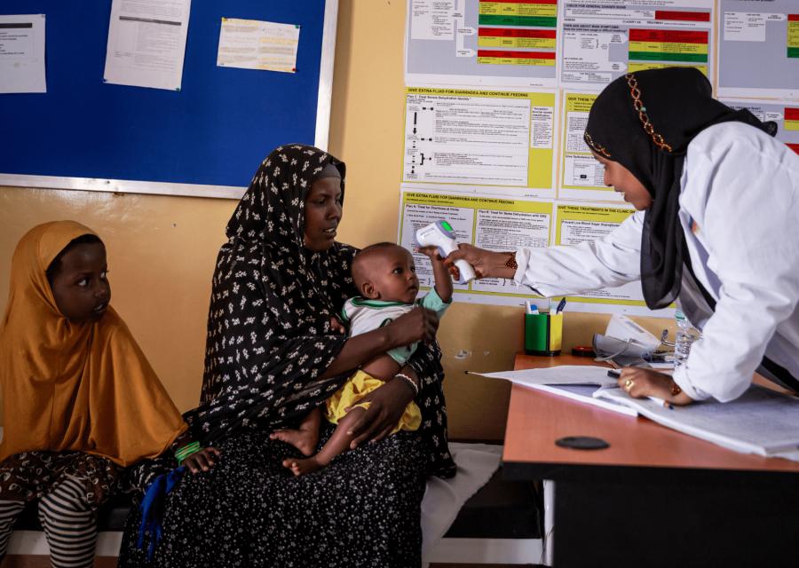 Operatrice Save the Children che prende la temperatura ad un bambino mentre è in braccio alla madre