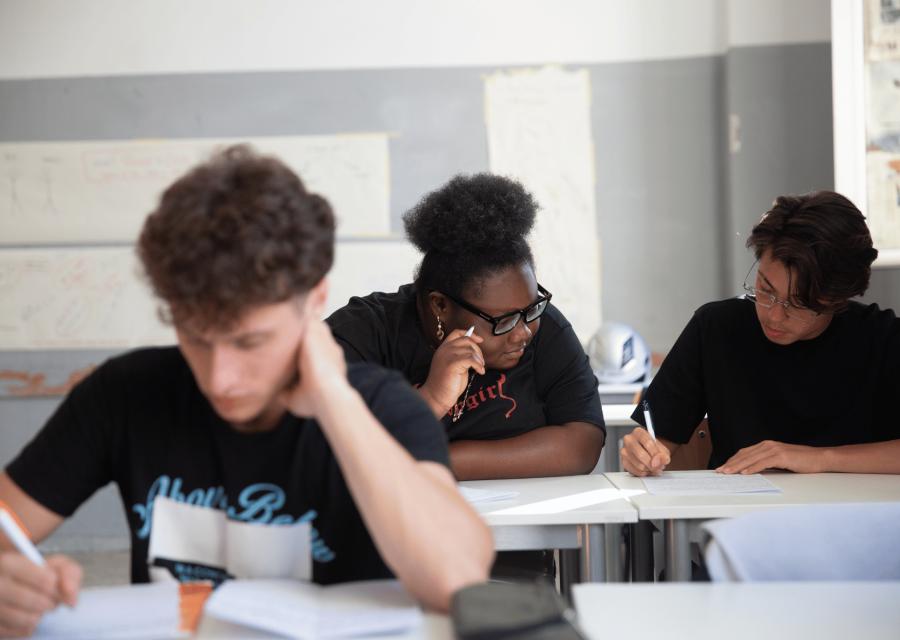 Tre studenti al banco di scuola che scrivono