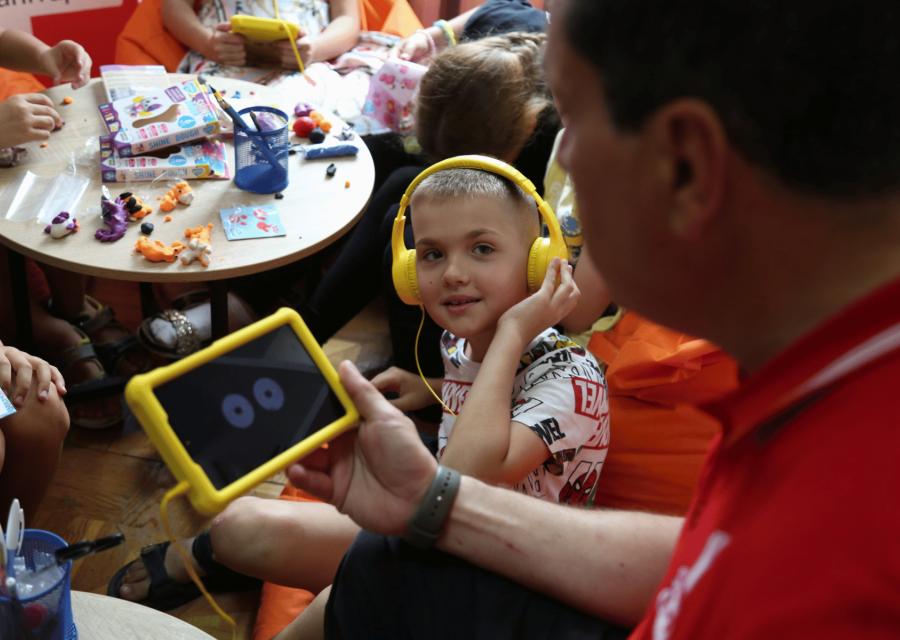 Bambino con cuffie che guarda un adulto accanto a lui con cellulare in mano 