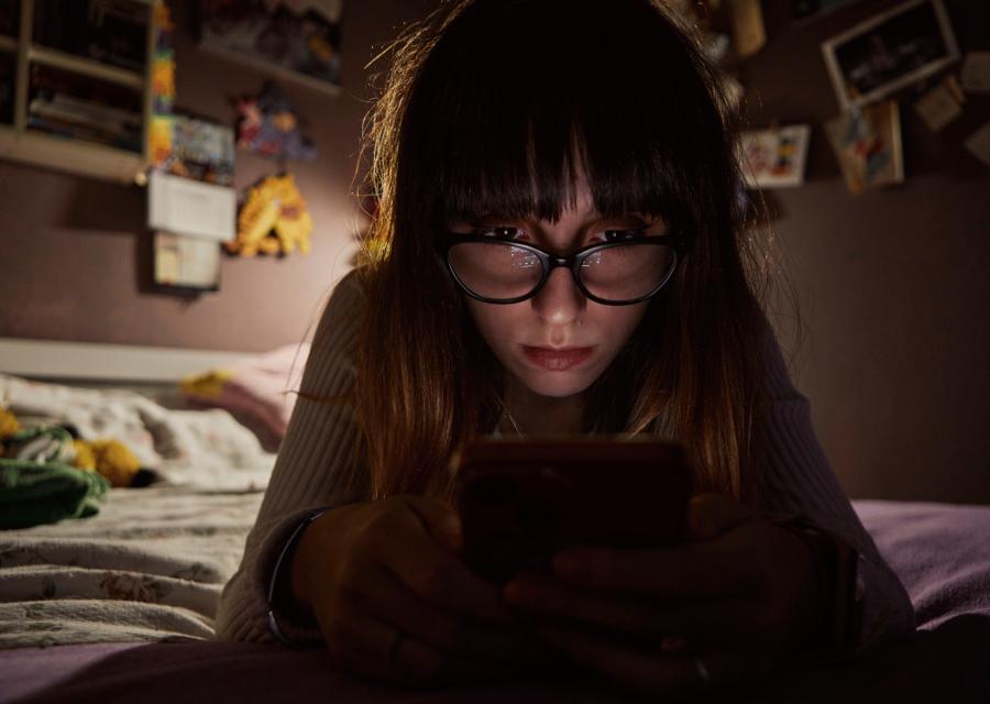 Ragazza al buio che guarda lo schermo del suo telefono.