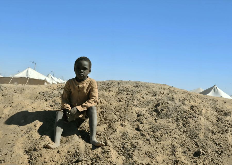 bambino seduto per terra vicino a campo di rifugiati