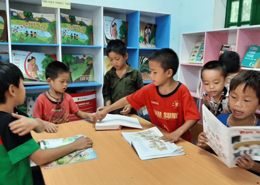 Sei bambini seduti intorno a un tavolo che leggono libri di scuola 