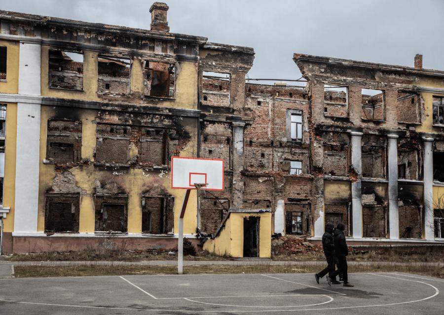 Ragazzi che camminano in un campo da basket con palazzo distrutto alle spalle