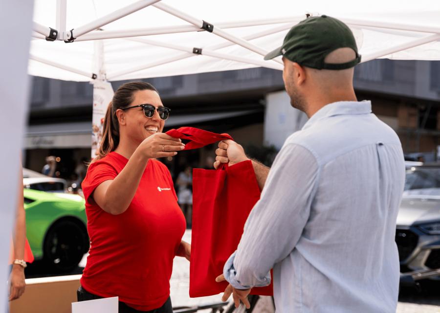 Volontaria Save the Children che passa borsa rossa a un donatore