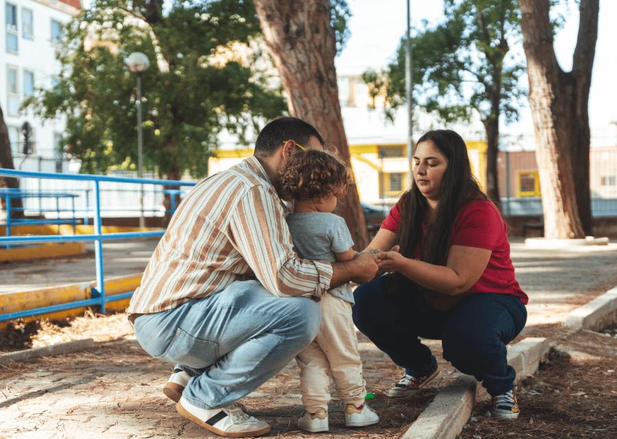 Padre e madre in ginocchio di fronte a figlio piccolo in un parchetto 