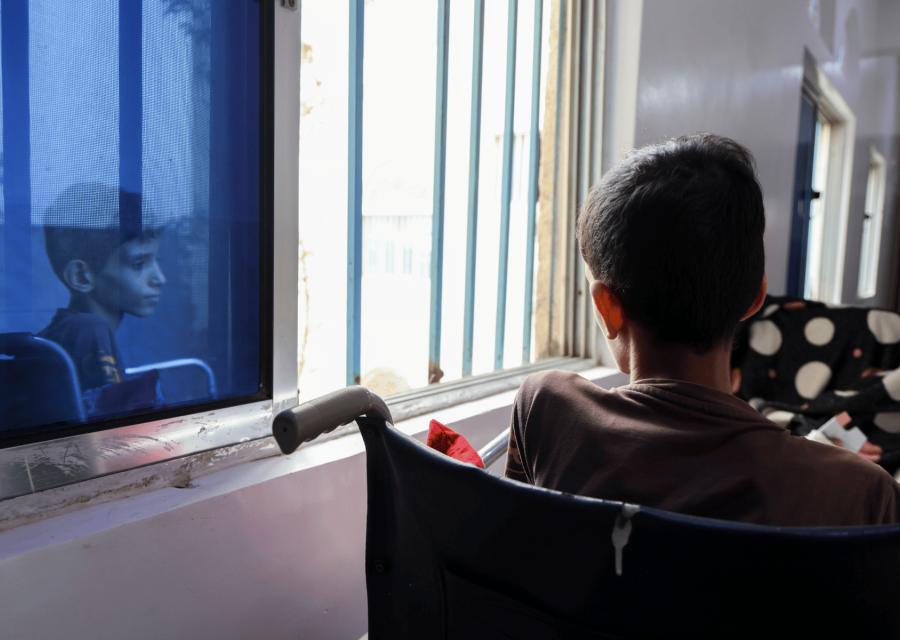 Bambino seduto su una sedia a rotelle con il riflesso del viso sulla finestra.