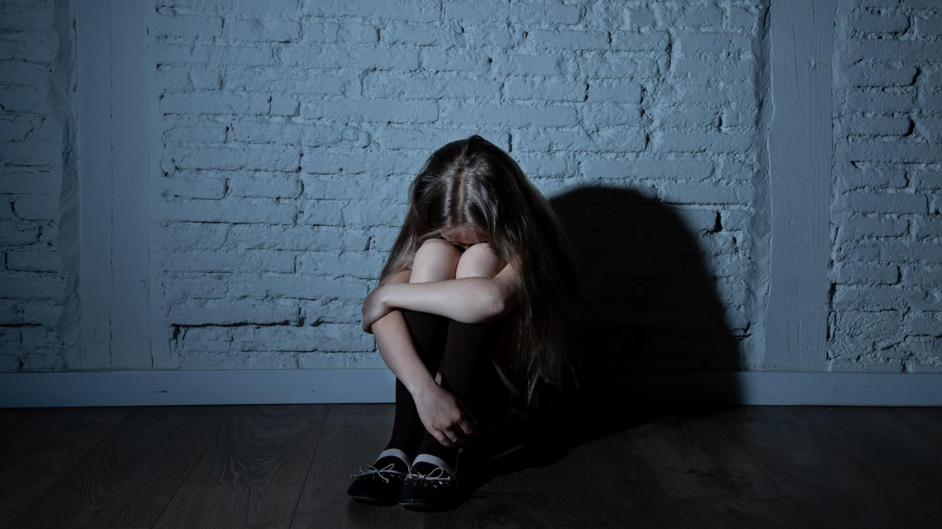 bambina davanti a un muro seduta accovacciata con la testa fra le braccia