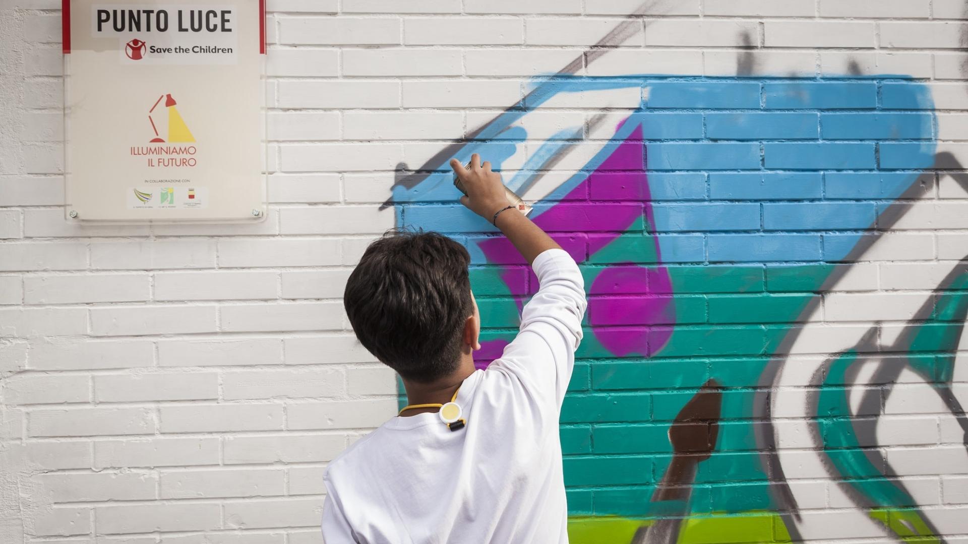 bambino al di fuori di un punto luce di save the children italia disegna un murales