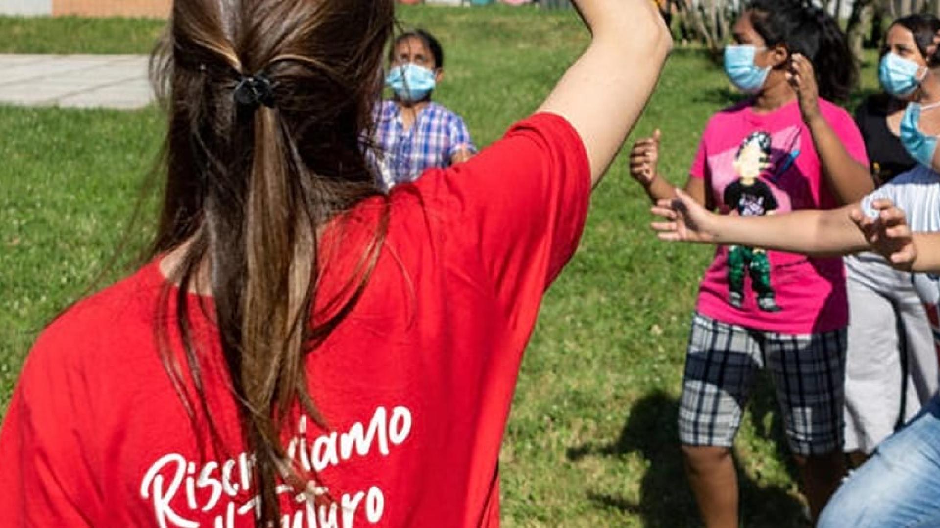 Un'operatrice Save the Children gioca in un prato con alcuni bambini 