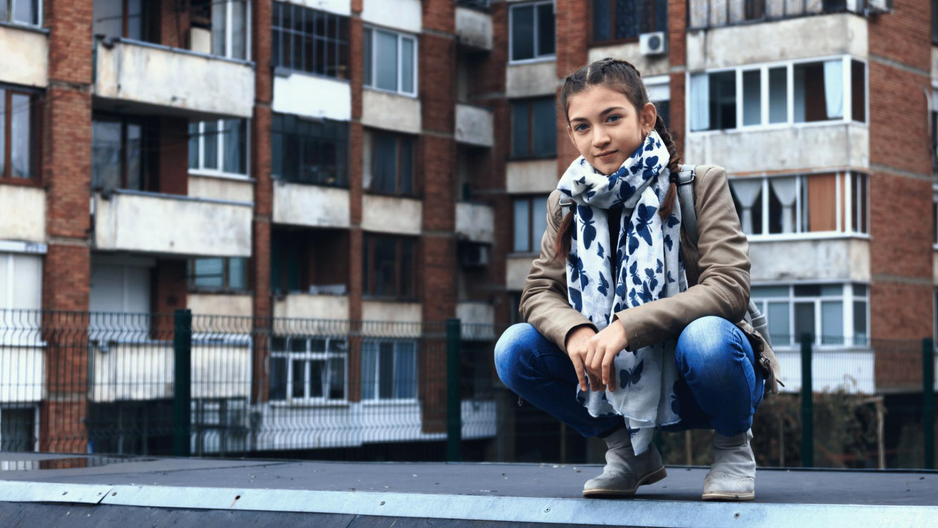 Bambina accovacciata davanti ad alcuni palazzi di periferia