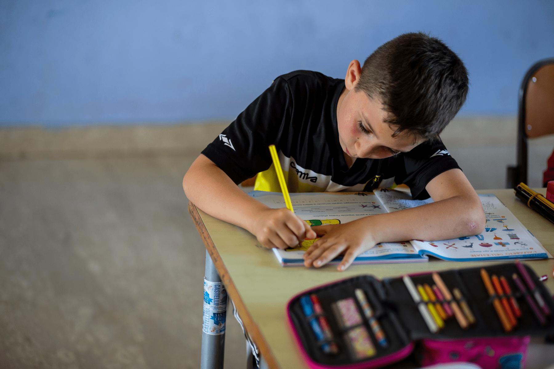 Bambino che scrive su un quaderno sui banchi di scuola