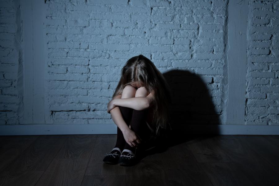 bambina davanti a un muro seduta accovacciata con la testa fra le braccia