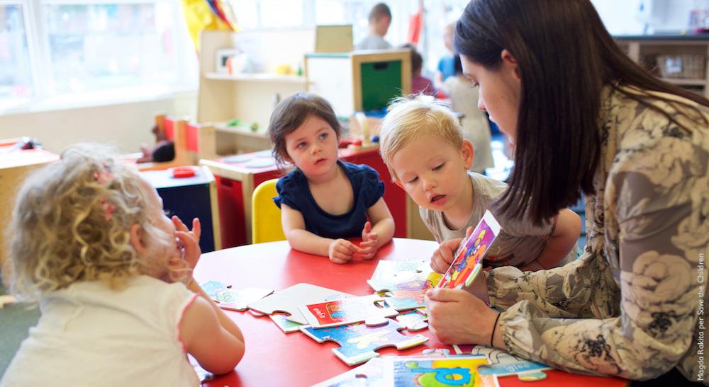 Insegnante d'asilo con tre bambini fanno i compiti al tavolo