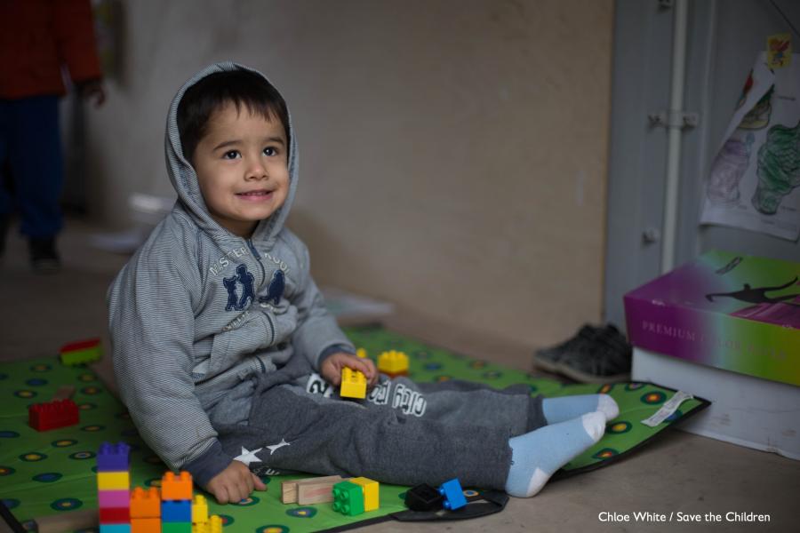 bimbo con felpa con cappuccio seduto per terra su un tappeto dei giochi con giochi intorno a sè