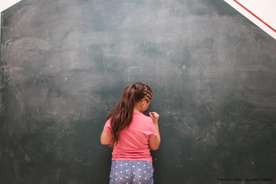 bambina alla lavagna girata di spalle scrive con un gessetto