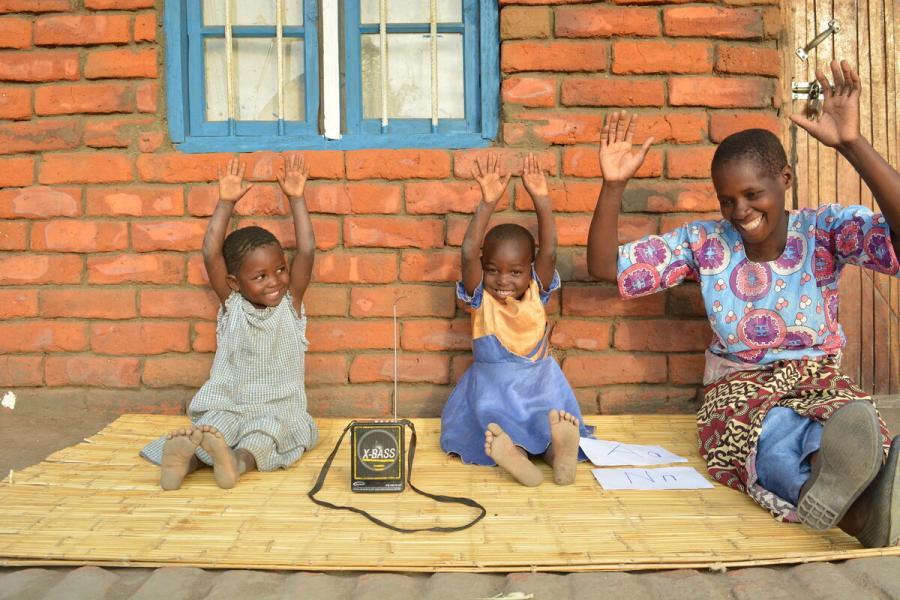 3 bambini di età diverse seduti a terra con le mani alzate e sorridenti 