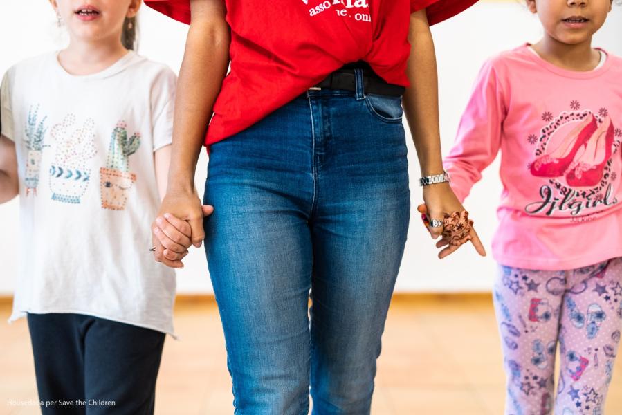 Operatrice Save the Children che tiene per mano due bambine a destra e sinistra