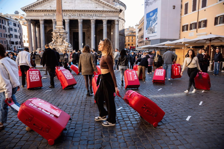Ragazza in primo piano con valigia in piazza al Pantheon insieme ad altri ragazzi con la valia